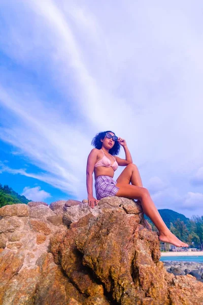 岩の形成に座っている魅力的な女性の垂直低角度ショット日焼けを取得 — ストック写真