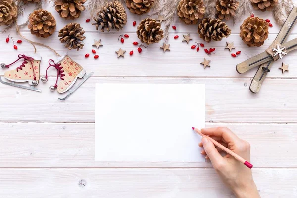 Scrittura a mano su una carta con una matita rossa circondata da decorazioni natalizie su un tavolo di legno — Foto Stock