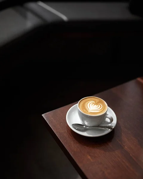 Wysoki kąt ujęcia filiżanki cappuccino ze sztuką kawy na drewnianej powierzchni — Zdjęcie stockowe