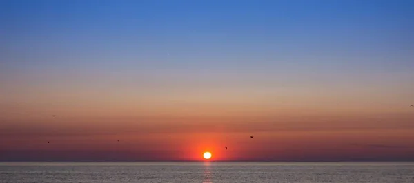 Impresionante paisaje de puesta de sol con colores cálidos que se reflejan en el océano —  Fotos de Stock