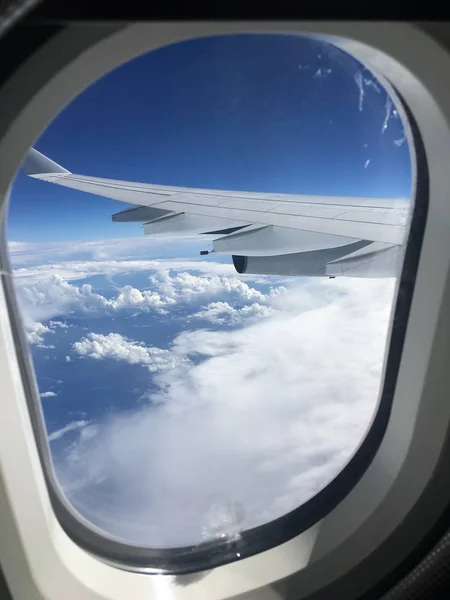 A picture of a plane wing from the plane window still in the air with blue sky and clouds