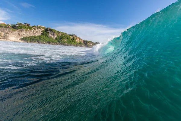 Close-up van een zeegolf omgeven door bergen en groen onder een blauwe lucht in Uluwatu in Bali — Stockfoto