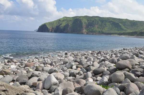 Vista de una playa llena de piedras blancas con una colina alta en el fondo bajo un cielo azul — Foto de Stock