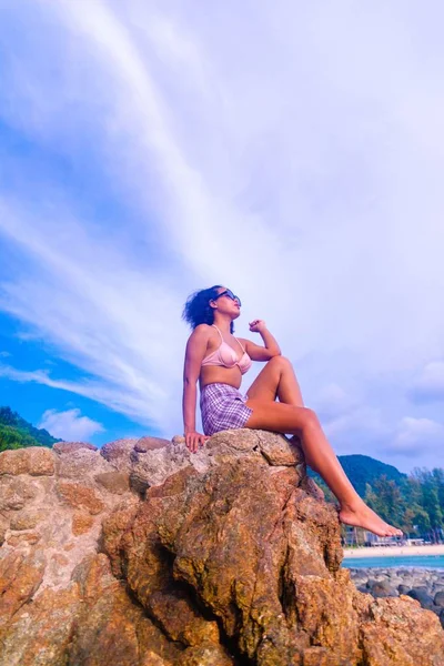 岩の形成に座っている魅力的な女性の垂直低角度ショット日焼けを取得 — ストック写真