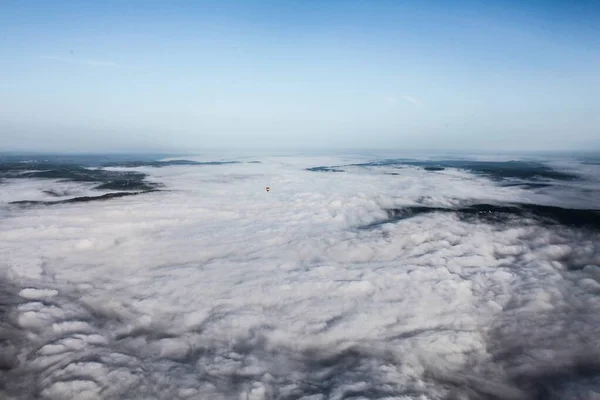 Tiro de ângulo alto das nuvens brancas sobre as montanhas e um pequeno balão de ar voando — Fotografia de Stock