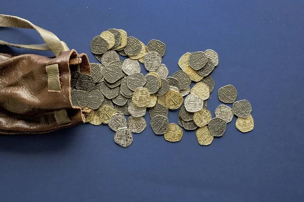 Primer plano de monedas viejas derramadas de la bolsa sobre una superficie azul oscuro — Foto de Stock