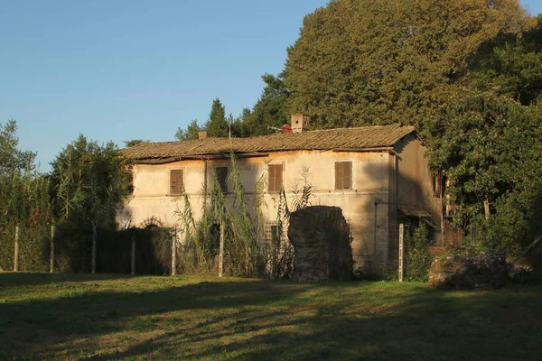 Vecchia casa con pareti sporche circondata da alberi ed erba sotto un cielo blu — Foto Stock