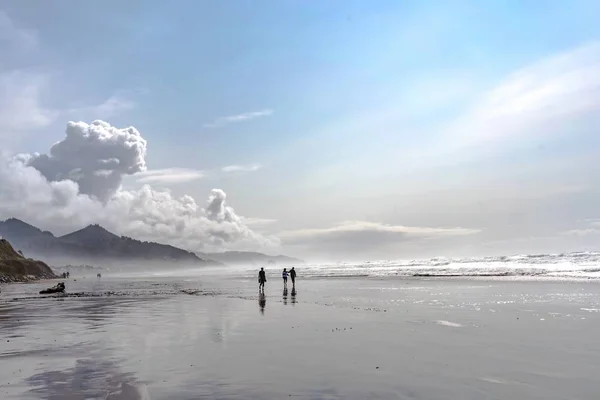 Strand med människor som går på den med havet och bergen på bakgrunden under en molnig himmel — Stockfoto