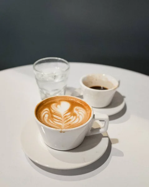 Plan vertical d'une table basse avec une tasse de cappuccino, un verre d'eau et un café à moitié bu — Photo