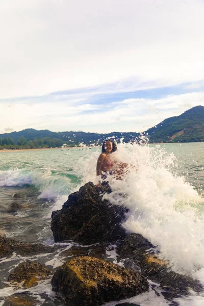 Pionowe Ujęcie Szczęśliwej Kobiety Siedzącej Skale Cieszącej Się Falami Oceanicznymi — Zdjęcie stockowe