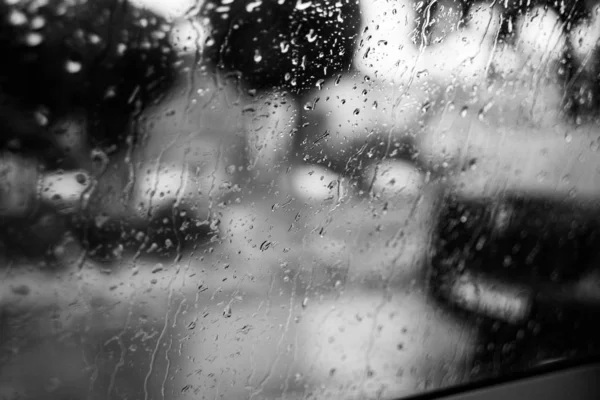 Plan en échelle de gris d'un verre recouvert de gouttes de pluie avec un fond flou — Photo