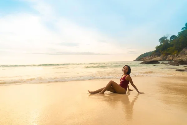 日の出の間砂浜に座っている赤い水着を着た魅力的な女性 — ストック写真