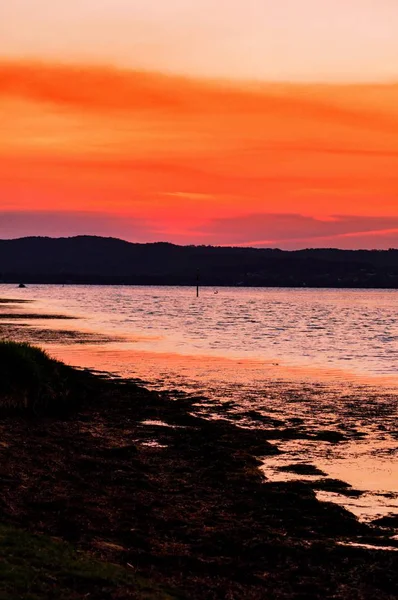 Vertical shot of the beach and the ocean under the colorful sky — Stock Photo, Image