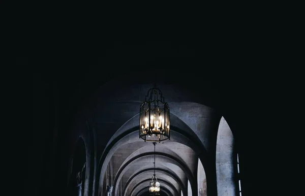 Low angle shot of beautiful chandeliers on the ceiling on a dark arch shaped hallway — Stock Photo, Image