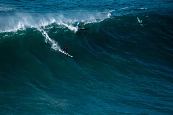 Ola alta del Océano Atlántico llevando a los surfistas hacia la orilla del Nazare, Portugal —  Fotos de Stock