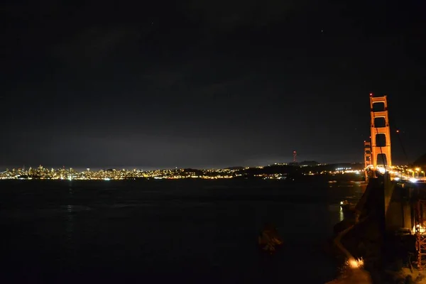 夜色中的金门大桥，城市的灯光反射在背后的水面上 — 图库照片
