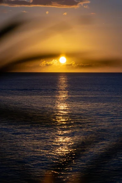 Завораживающий вертикальный снимок заходящего солнца за облаками над спокойным океаном — стоковое фото