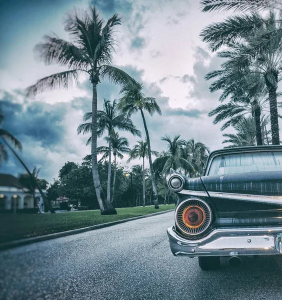 Närbild av en vintage bil på vägen omgiven av palmer och byggnader under en molnig himmel — Stockfoto