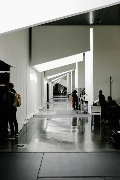 Vertical shot of people in a hallway with white illuminated ceiling — Stock Photo, Image
