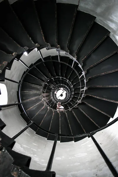 Laaghoekige opname van een persoon die neerkijkt vanaf een zwarte spiraalvormige trap met metalen rails — Stockfoto