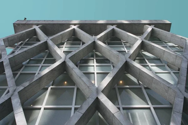 Mavi gökyüzünün altındaki çimento binanın geometrik cephesinin alçak açılı görüntüsü. — Stok fotoğraf