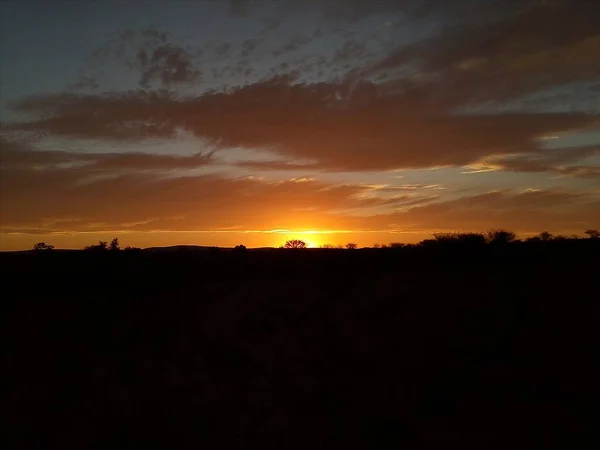 Breathtaking view of the sunset in the cloudy sky above the silhouette of a land — Stock Photo, Image