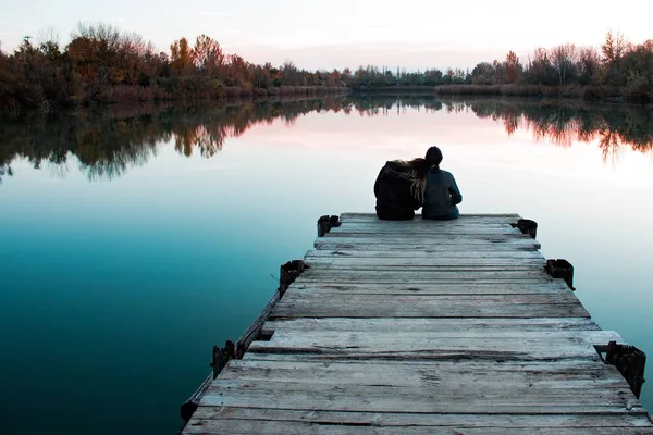 Amis assis sur un quai en bois avec l'un d'eux reposant sa tête sur l'épaule près de la mer — Photo