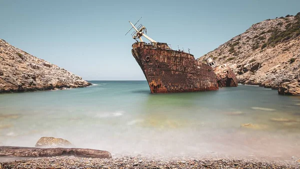 Abandoned rusty ship in the sea near huge rock formations under the clear sky
