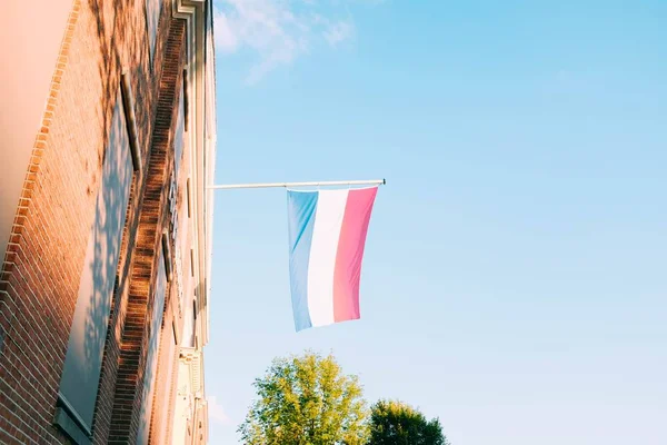 Nízký úhel záběru vlajky Nizozemska na cihlové budově pod modrou oblohou — Stock fotografie