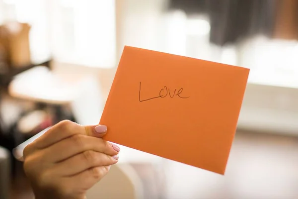 Πρόσωπο με πορτοκαλί κάρτα με τη λέξη Αγάπη γραμμένη πάνω της — Φωτογραφία Αρχείου