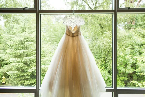 Hermoso vestido de novia blanco colgando en una ventana con los árboles verdes en el fondo — Foto de Stock