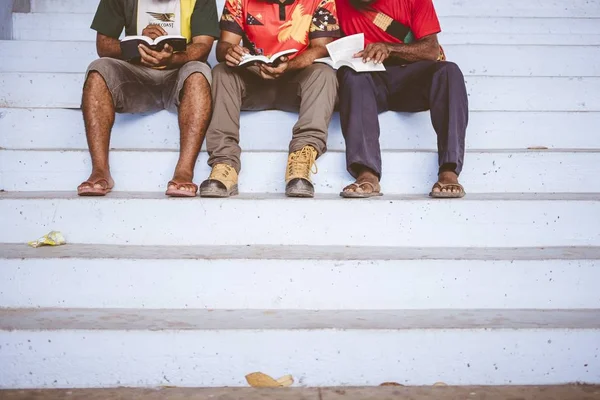 Drie mannen zitten naast elkaar op de trap terwijl ze de bijbel lezen. — Stockfoto