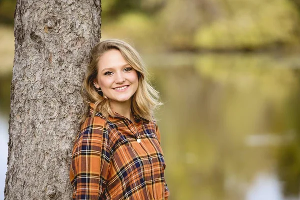 木にもたれてカメラで微笑む美しい女性の浅い焦点のショット — ストック写真
