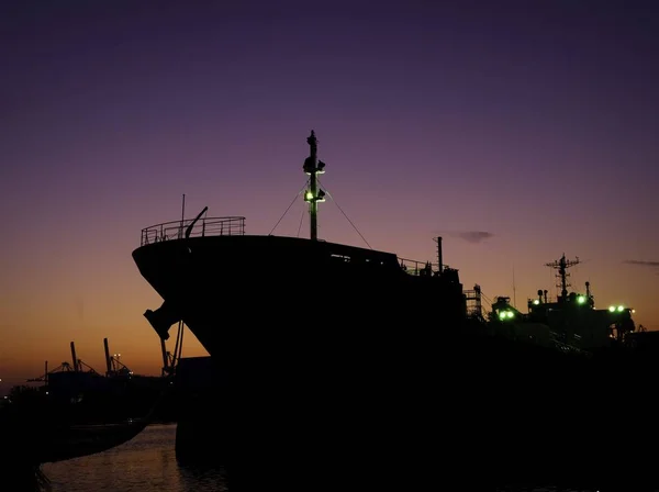 The silhouette of a giant ship with green lights and the colorful sky in the background