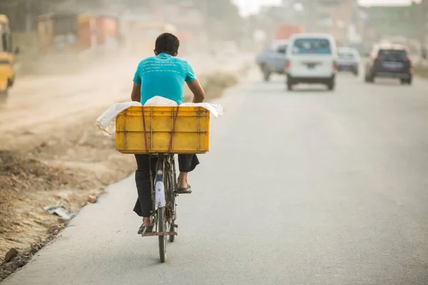 Trabajador simple montando una bicicleta que lleva una caja pesada con buenos coches delante de él —  Fotos de Stock