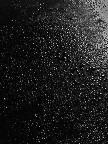 Vertikale Graustufenaufnahme von Wassertropfen auf einem schwarzen Tisch — Stockfoto