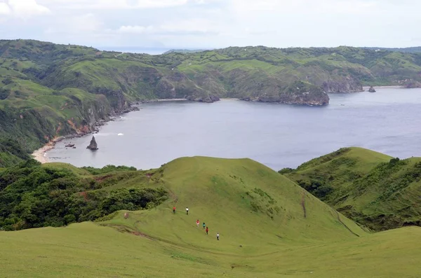Grupo de personas recorriendo las montañas alrededor de un mar rodeado de vegetación bajo un cielo azul —  Fotos de Stock