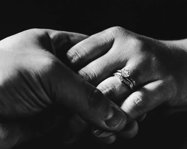 Encerramento greyscale de segurar as mãos com um anel de casamento contra um fundo preto — Fotografia de Stock