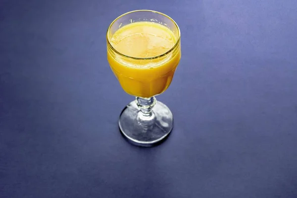 High angle shot of an orange juice in a glass on a dark blue surface — Stock Photo, Image