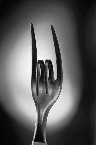 Tiro vertical a escala de grises de un tenedor de metal doblado que simboliza el signo de la música rock —  Fotos de Stock