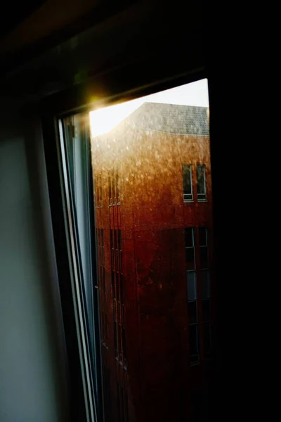 Tiro vertical de uma janela testemunhando o nascer do sol sobre a cidade — Fotografia de Stock