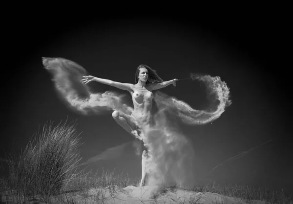 Снимок в оттенках серого привлекательной голой женщины, танцующей на песке и брызгающей песком в воздух Лицензионные Стоковые Фото