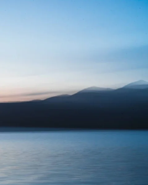 Serene uitzicht op een rustige oceaan omgeven door de donkere silhouetten van de bergen onder een heldere hemel — Stockfoto