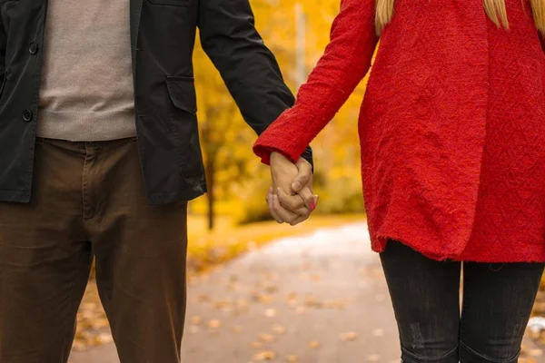 A couple holding hands walking through a road in a park surrounded by trees on the background