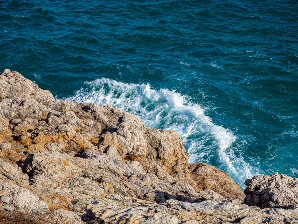 Nice scape of the blue ocean waves meeting the brown cliffy rocks on the shore