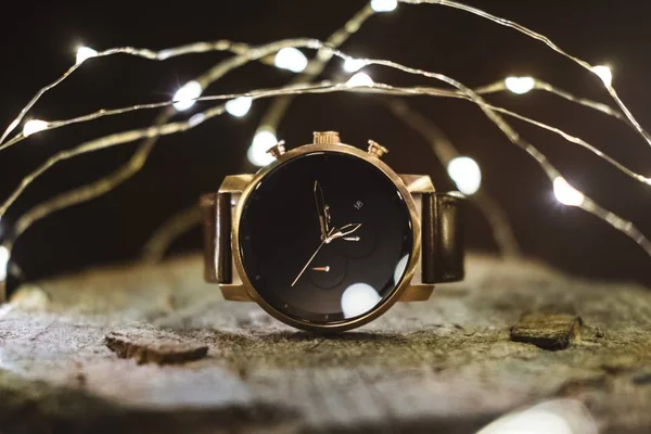 背景にライトのチェーンを持つ木製の表面に配置された手の時計のクローズアップショット — ストック写真