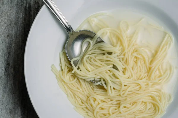 Primer plano en ángulo alto de espaguetis hervidos caseros con leche en un plato blanco —  Fotos de Stock