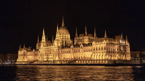 Parlamento de Budapeste iluminado ao lado do rio à noite — Fotografia de Stock
