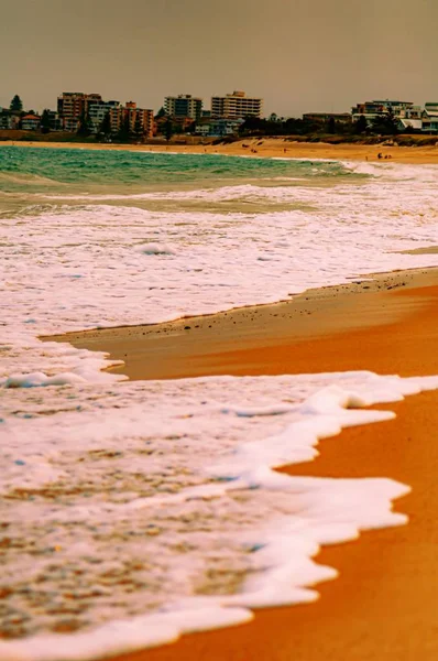 海岸線のオレンジ色の砂に出会う白い波の魅惑的な垂直ショット — ストック写真