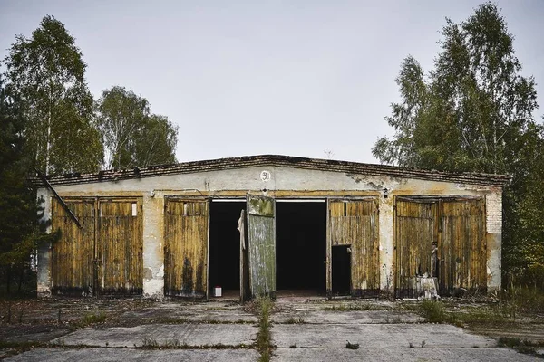 Antiguo almacén abandonado con puertas rotas rodeadas de árboles —  Fotos de Stock